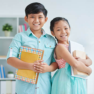 2 happy and successful Asian elementary students holding notebooks for school.